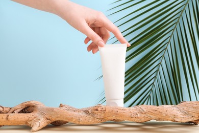 Woman with tube of cream and plant against light blue background, closeup