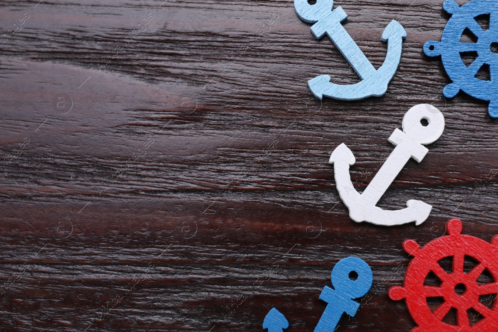 Photo of Anchor and ship wheel figures on dark wooden table, flat lay. Space for text