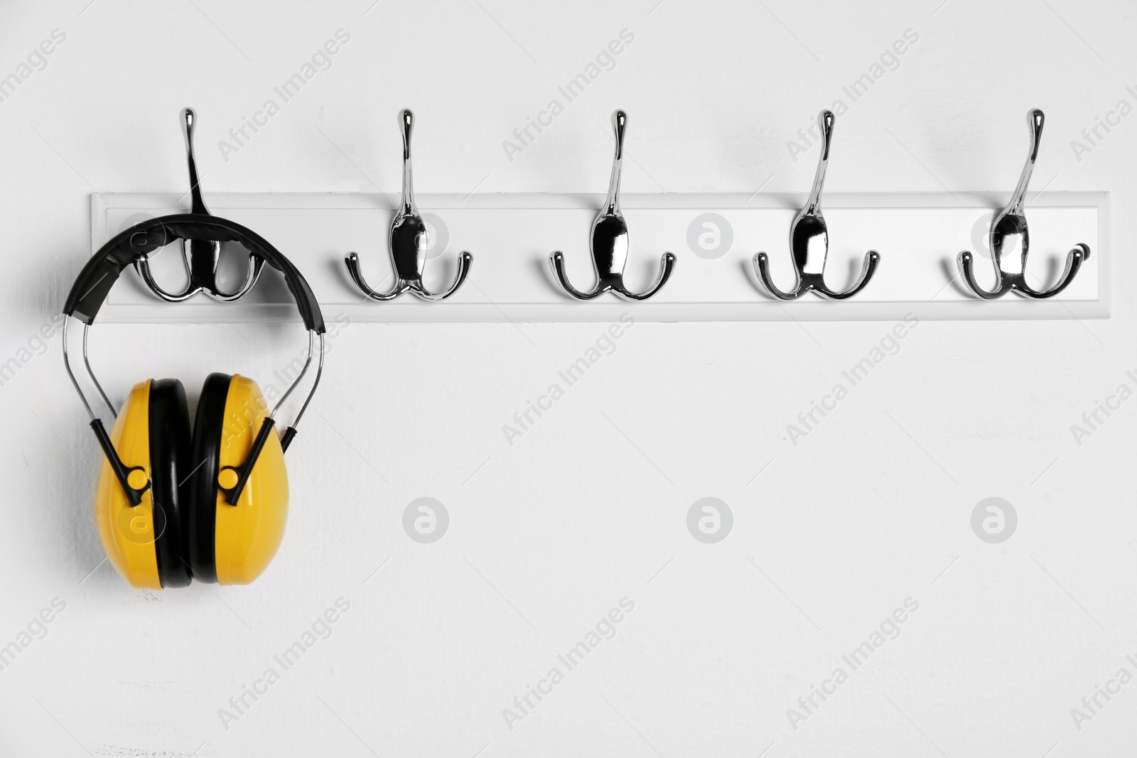 Photo of Protective headphones hanging on white wall. Safety equipment