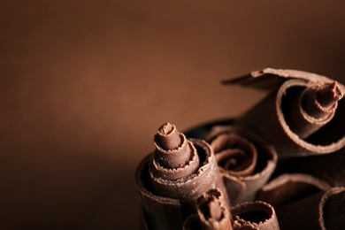 Photo of Curls of tasty dark chocolate against color background, closeup with space for text