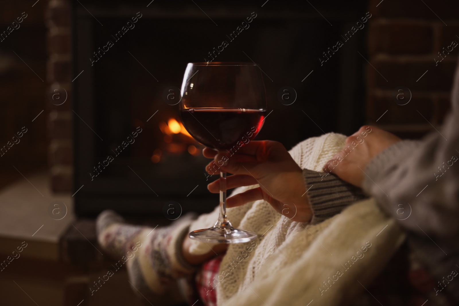 Photo of Woman with glass of red wine near burning fireplace, closeup