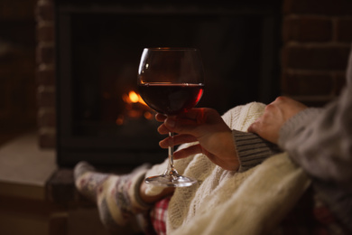 Woman with glass of red wine near burning fireplace, closeup
