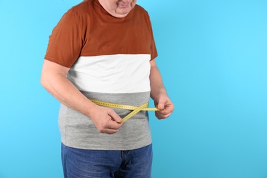 Fat senior man with measuring tape on color background, closeup. Weight loss