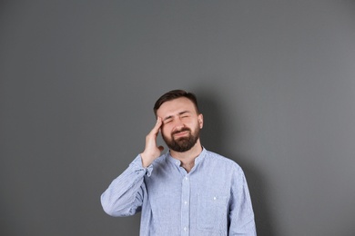 Portrait of handsome bearded man suffering from headache on color background