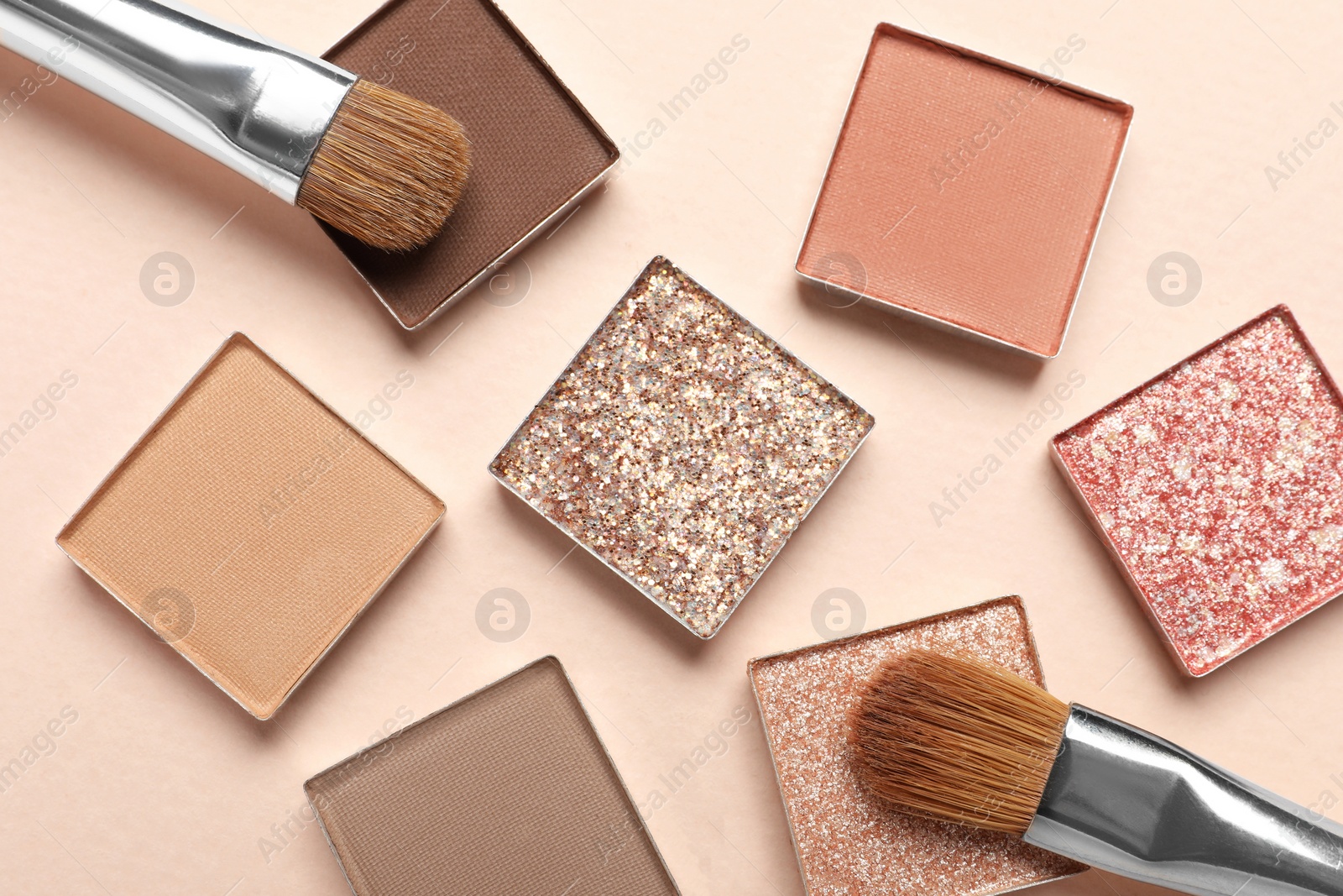 Photo of Different beautiful eye shadows and makeup brushes on beige background, flat lay