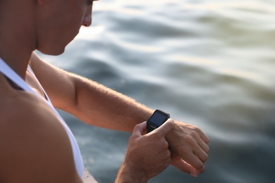 Man checking fitness tracker after training near river, closeup