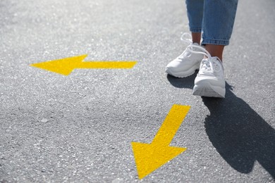 Image of Choice of way. Woman walking to drawn mark on road, closeup. yellow arrows pointing in different directions