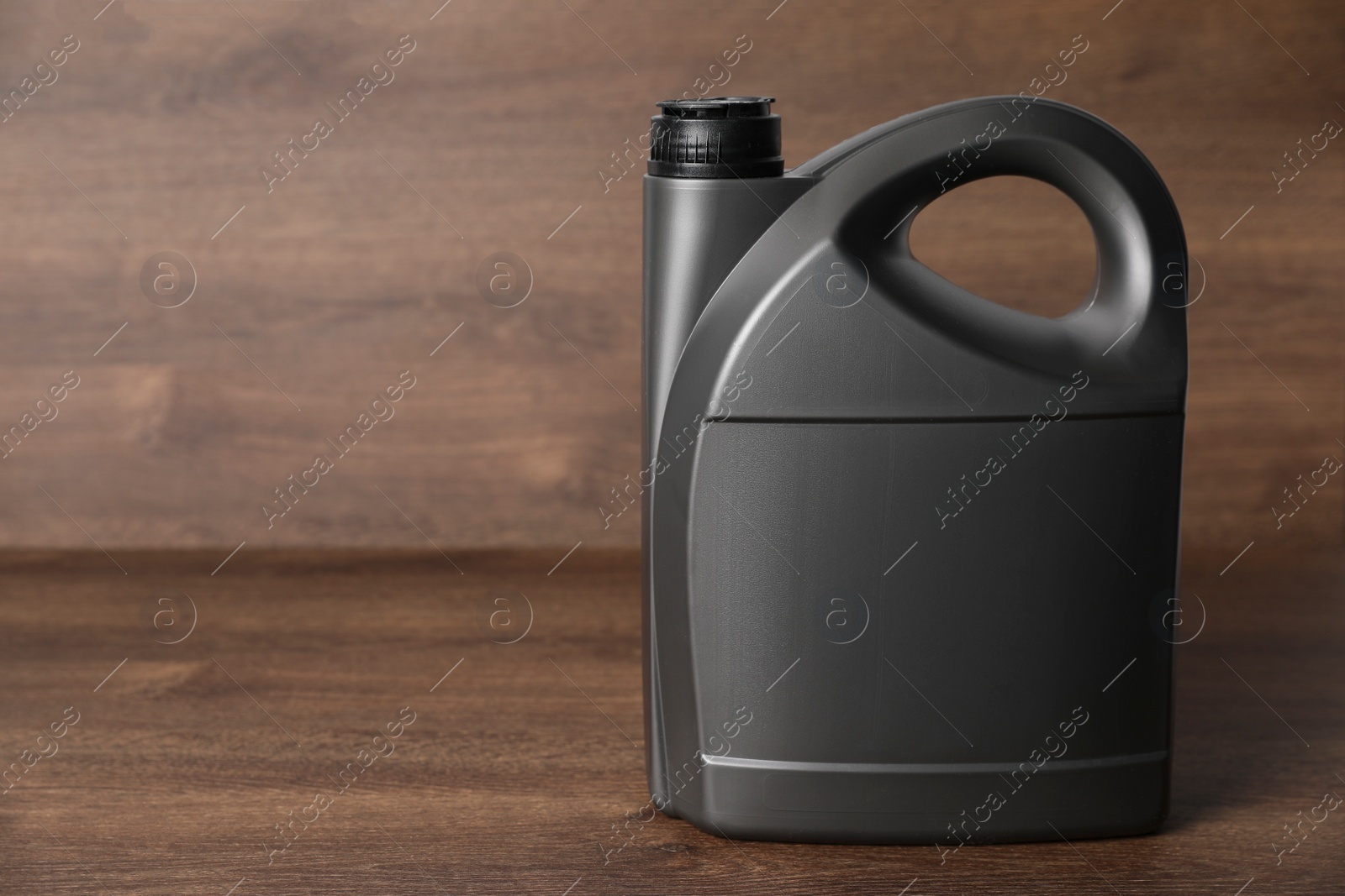 Photo of Motor oil in grey canister on wooden background, space for text