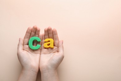 Photo of Woman holding calcium symbol made of colorful letters on beige background, top view. Space for text