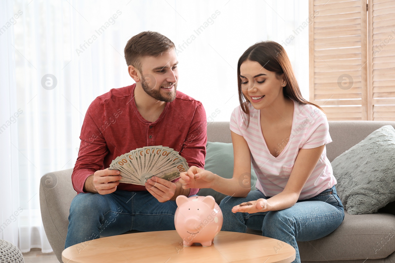 Photo of Beautiful young couple with piggy bank and money at home