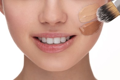 Teenage girl applying foundation on face with brush against white background, closeup