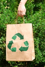 Photo of Woman holding paper bag with recycling symbol outdoors, closeup