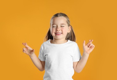 Photo of Child with crossed fingers on yellow background. Superstition concept