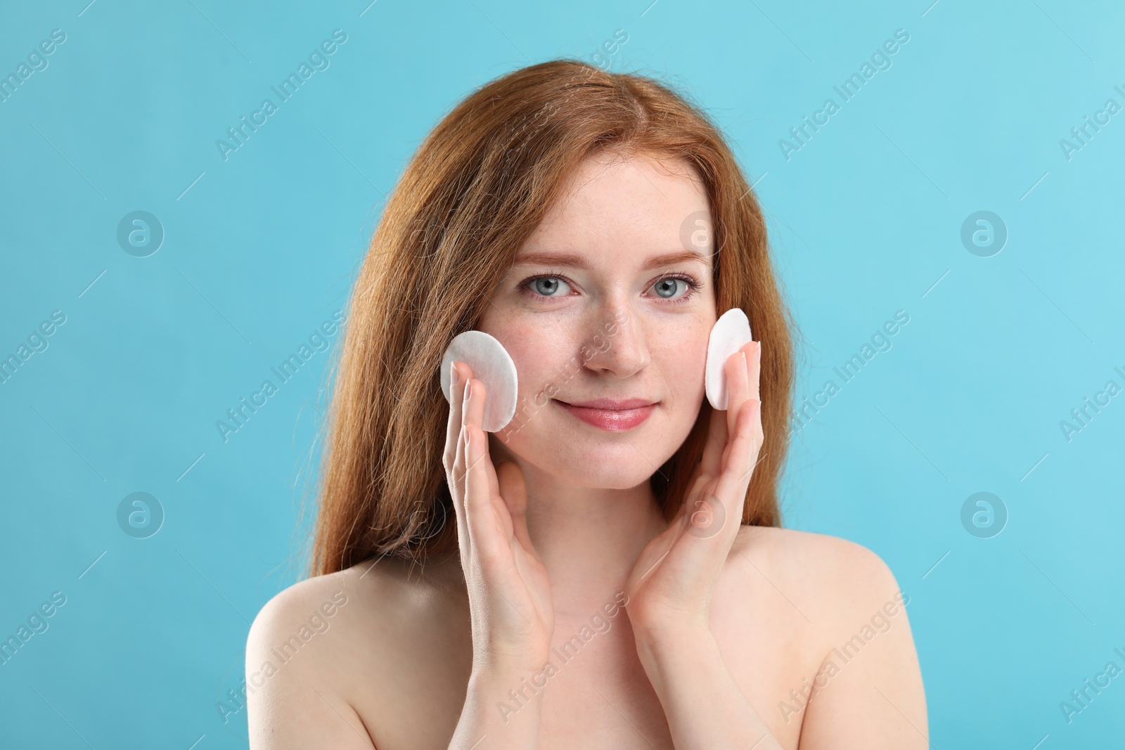 Photo of Beautiful woman with freckles wiping face on light blue background