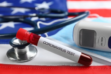 Test tube with blood sample, thermometer and stethoscope on American flag. Coronavirus pandemic in USA