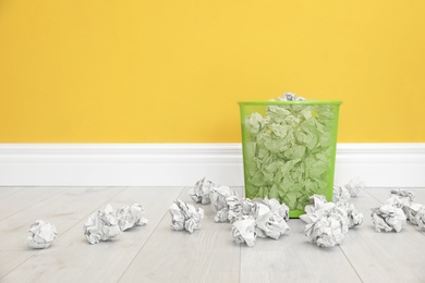 Metal bin with crumpled paper against color wall, space for text