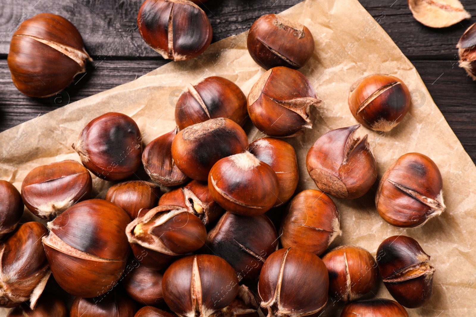 Photo of Tasty roasted edible chestnuts on black wooden table, top view