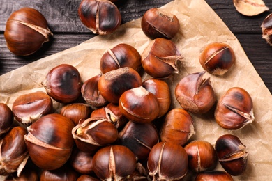 Photo of Tasty roasted edible chestnuts on black wooden table, top view