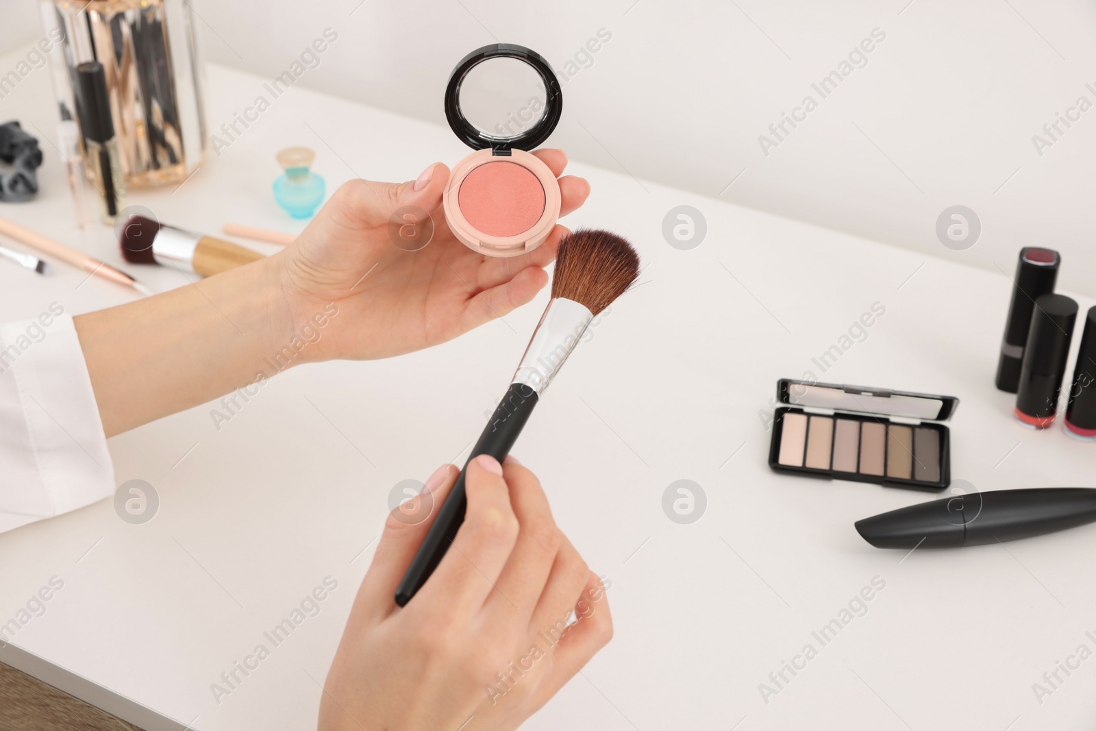 Photo of Woman with blusher and brush at dressing table indoors, closeup