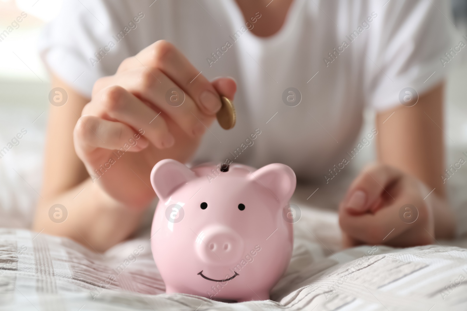 Photo of Woman putting money into piggy bank on bed at home, closeup