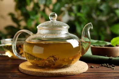 Glass teapot with fresh green tea on wooden table