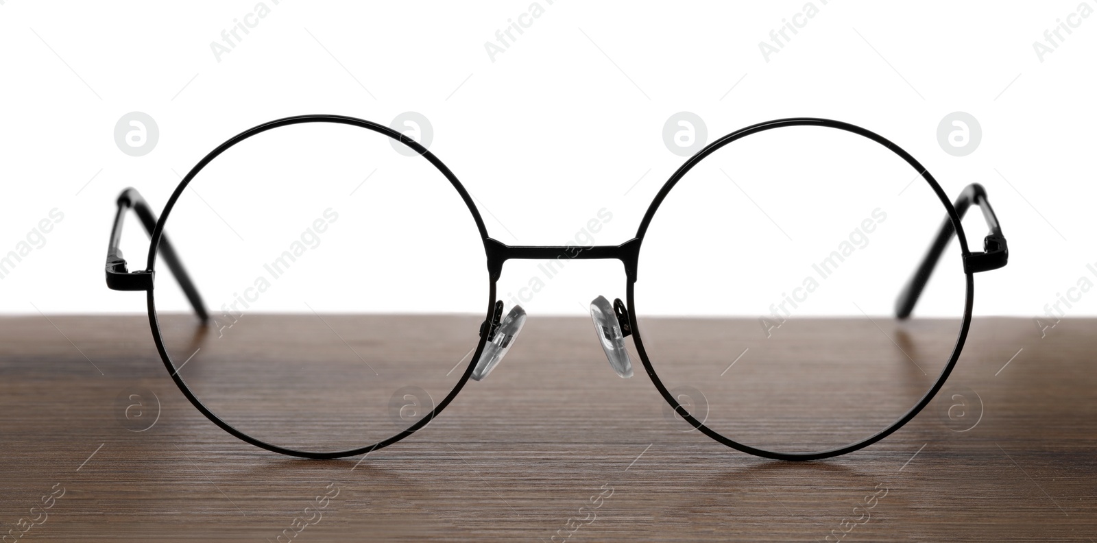 Photo of Round glasses with metal frame on wooden table against white background