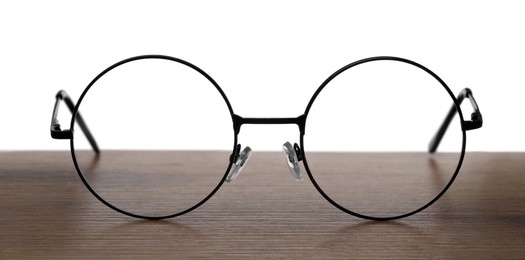 Photo of Round glasses with metal frame on wooden table against white background
