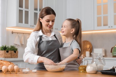 Photo of Making bread. Mother and her daughter kneading dough at wooden table in kitchen