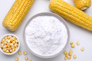 Photo of Bowl with corn starch, ripe cobs and kernels on white table, flat lay