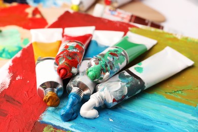 Photo of Tubes of colorful oil paints on canvas with abstract painting, closeup