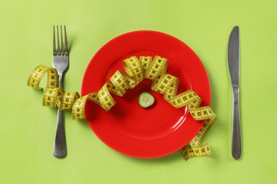 Photo of Plate with cucumber slice, cutlery and measuring tape on green background, flat lay. Diet concept