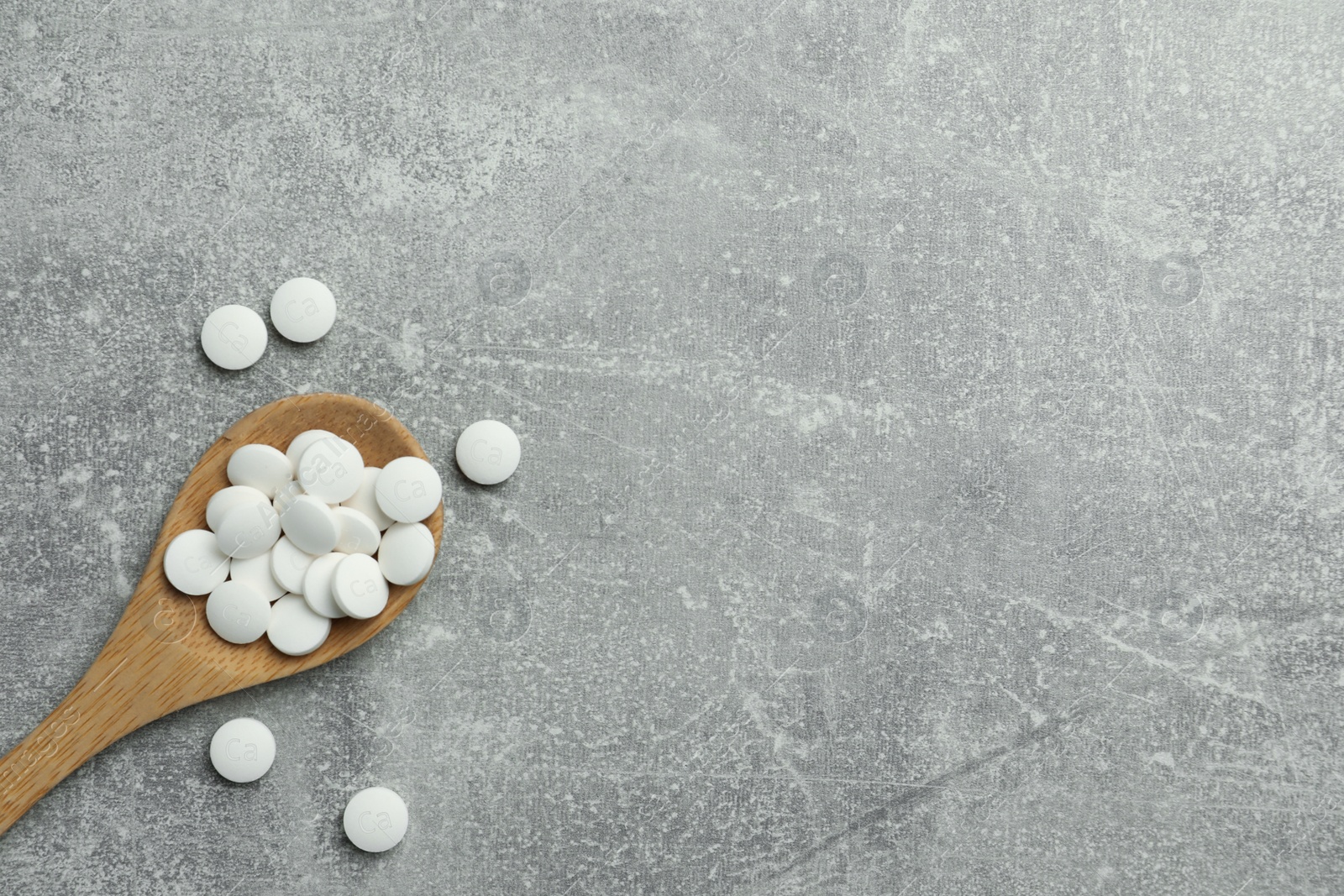 Photo of Calcium supplement pills and wooden spoon on grey table, flat lay. Space for text