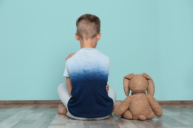 Photo of Little boy with toy sitting on floor near color wall in empty room. Autism concept