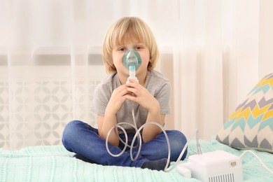 Photo of Sick little boy using nebulizer for inhalation on bed at home