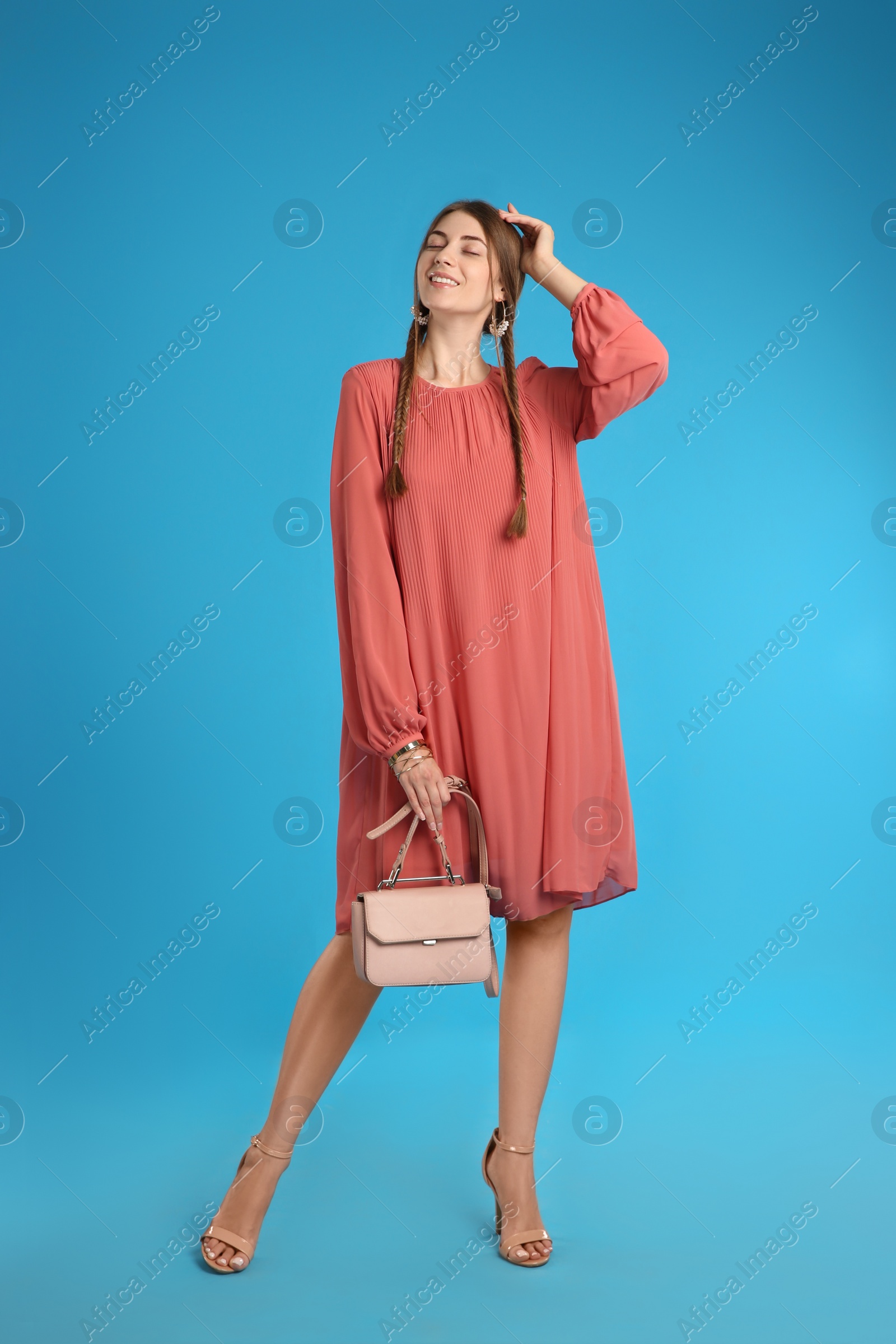 Photo of Beautiful young woman with stylish pink bag on light blue background