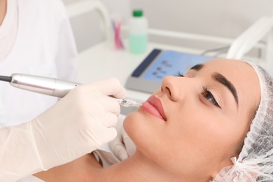 Young woman undergoing procedure of permanent lip makeup in tattoo salon, closeup