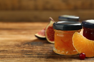 Jars of different jams and fresh ingredients on wooden table, space for text