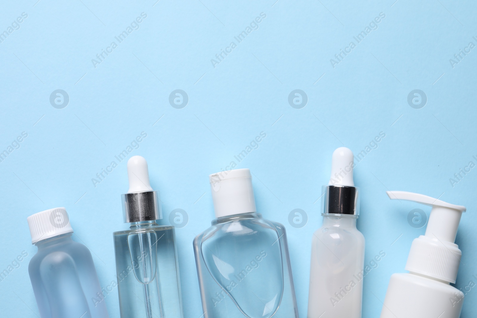 Photo of Many different bottles of cosmetic serum on light blue background, flat lay. Space for text