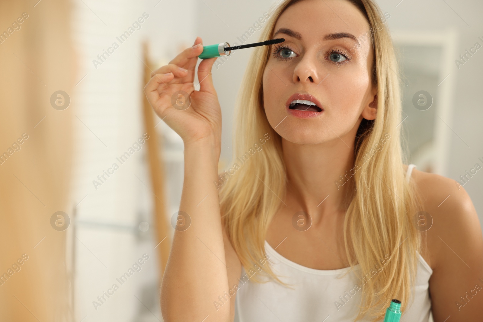 Photo of Beautiful woman applying mascara near mirror in bathroom