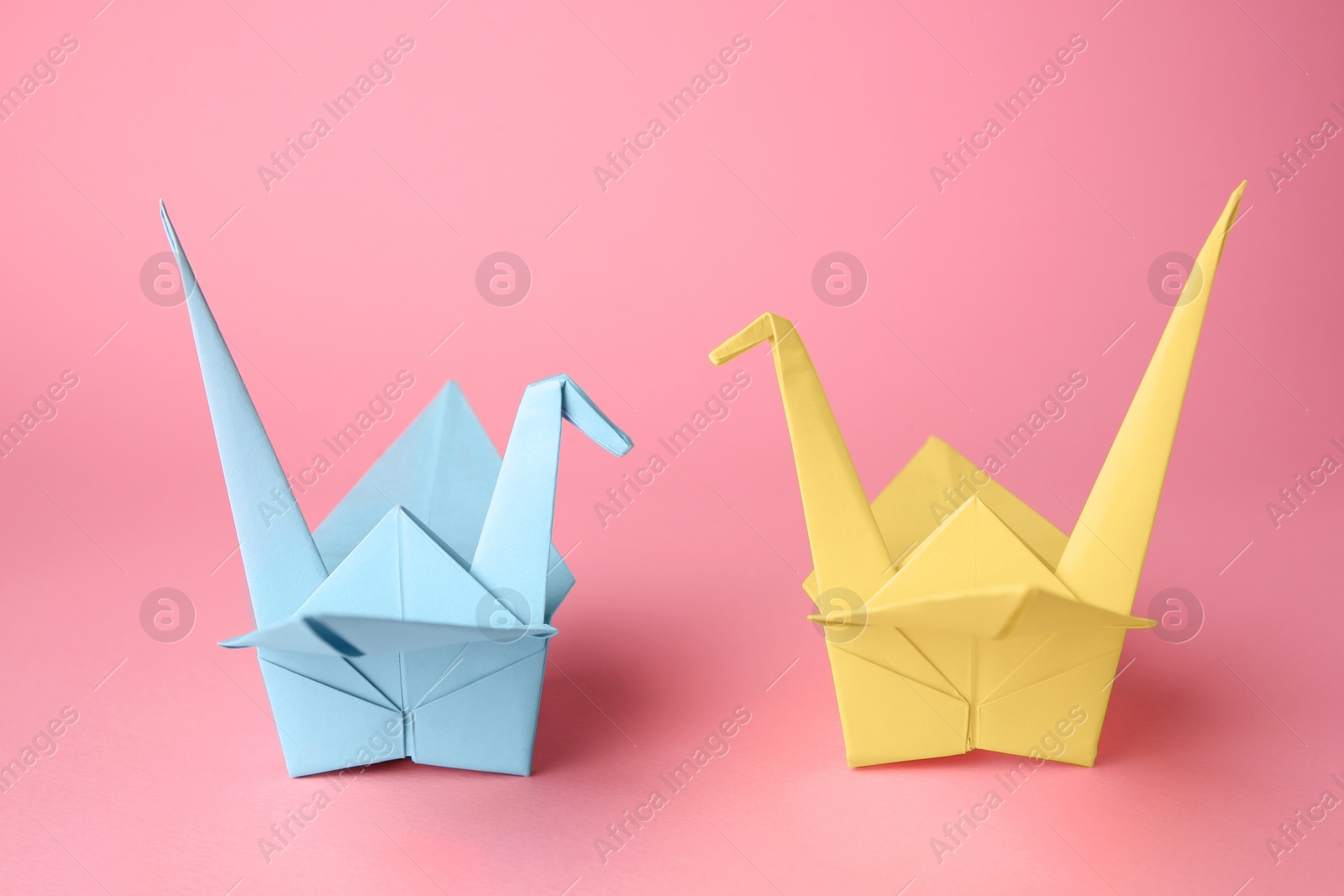 Photo of Origami art. Colorful handmade paper cranes on pink background