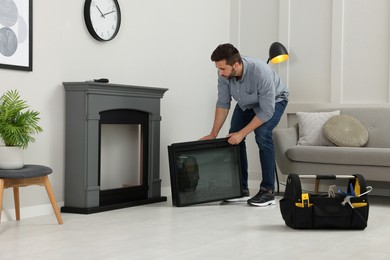 Man installing electric fireplace near wall in room