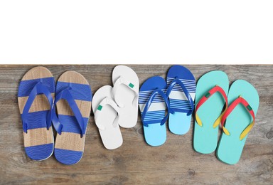 Photo of Pairs of bright flip flops on wooden table against white background, top view