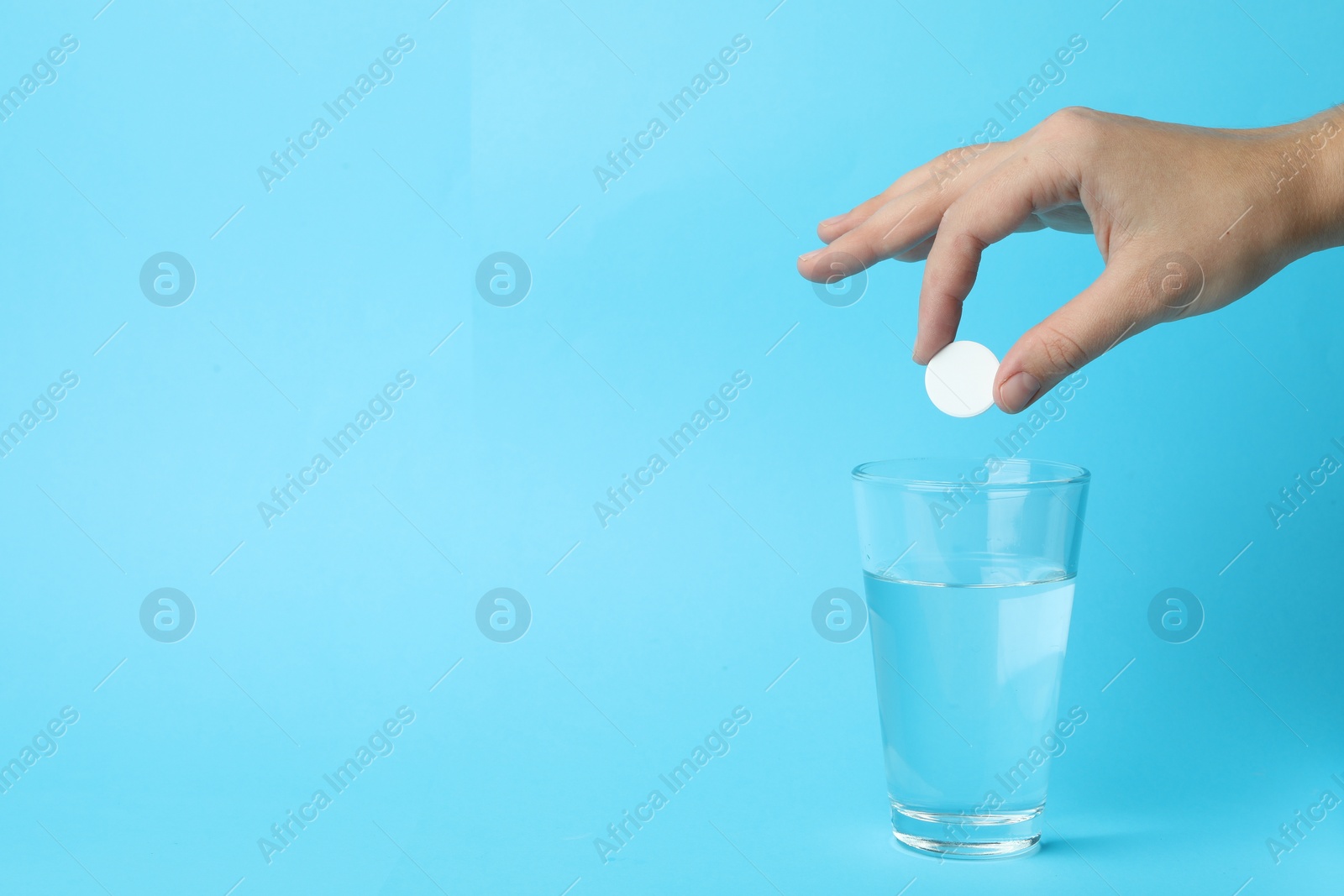 Photo of Woman putting tablet into glass of water on light blue background, space for text