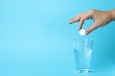 Photo of Woman putting tablet into glass of water on light blue background, space for text