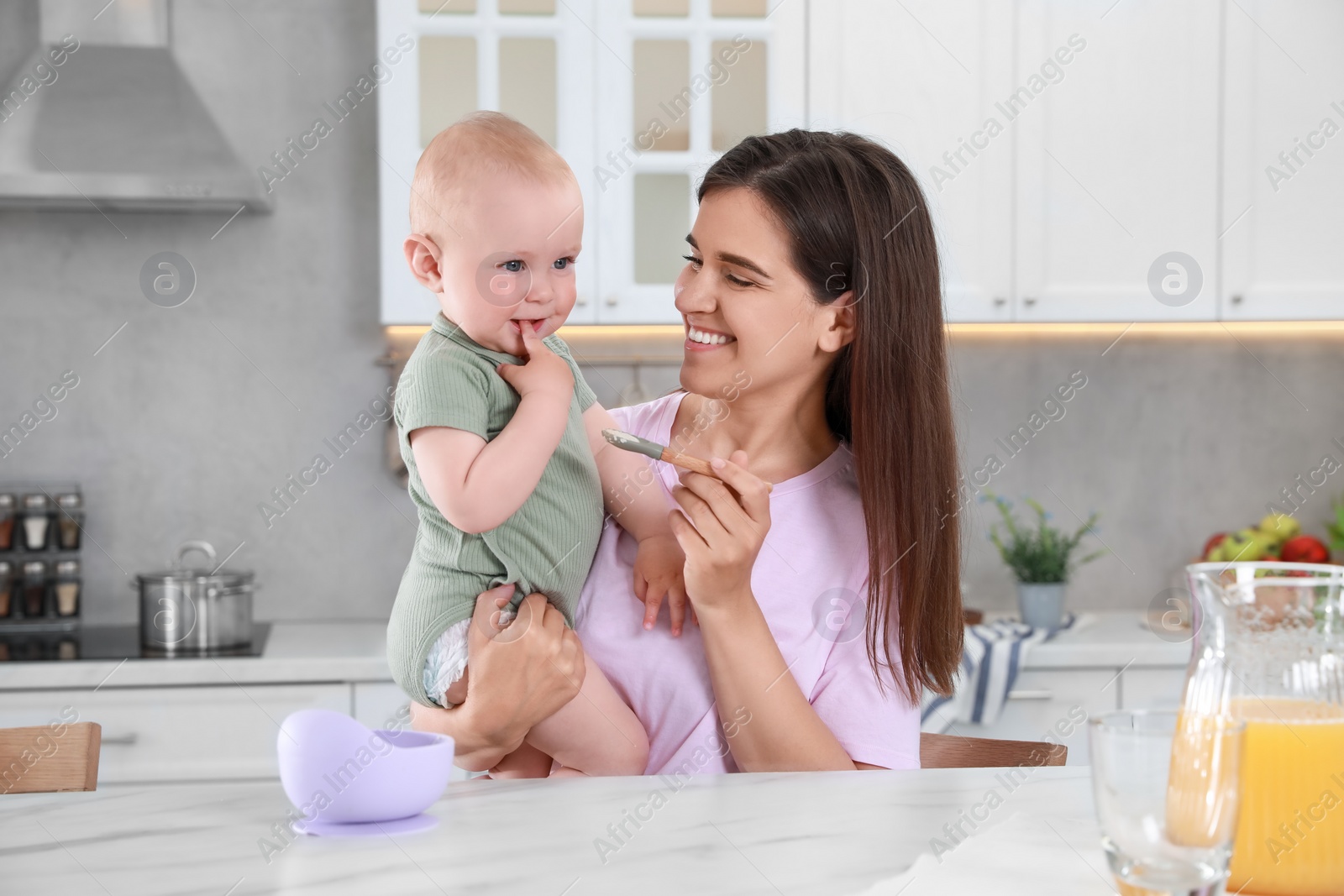 Photo of Happy young woman feeding her cute little baby at table in kitchen