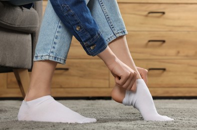 Photo of Woman putting on white socks at home, closeup