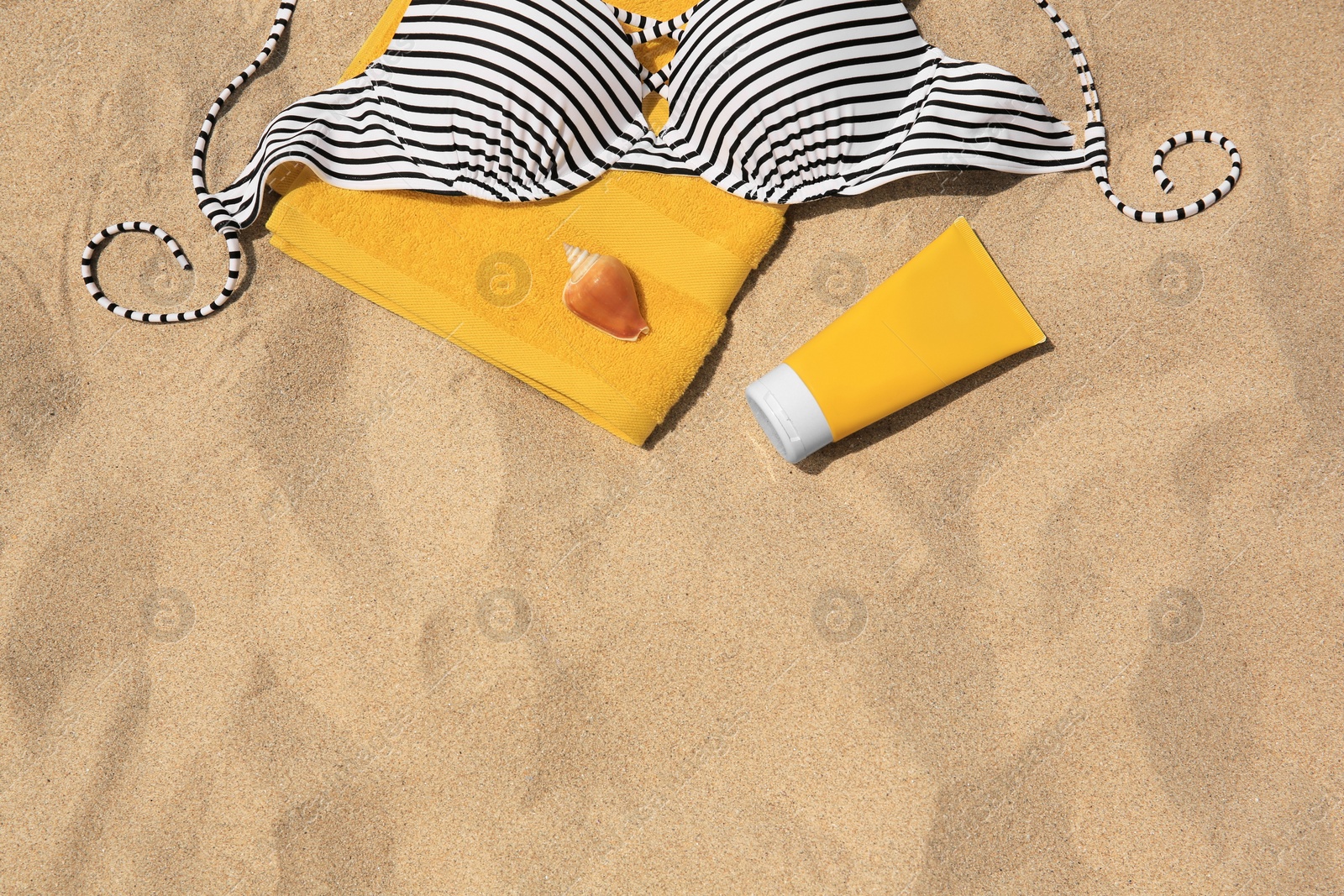 Photo of Sunscreen, towel, seashell and swimsuit top on sandy beach, flat lay and space for text. Sun protection