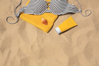 Photo of Sunscreen, towel, seashell and swimsuit top on sandy beach, flat lay and space for text. Sun protection
