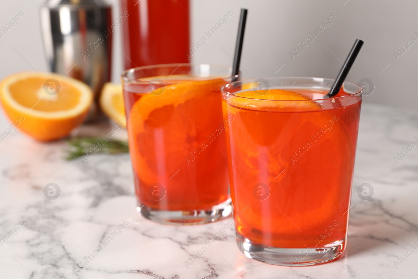 Photo of Aperol spritz cocktail, orange slices and straws in glasses on white marble table, closeup