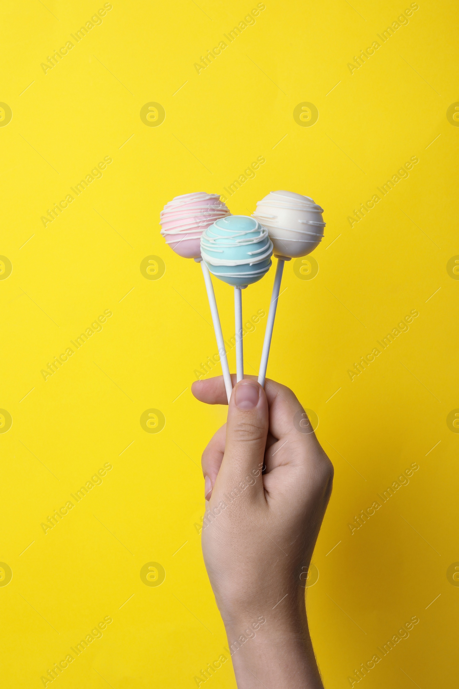 Photo of Woman holding sweet cake pops on yellow background, closeup